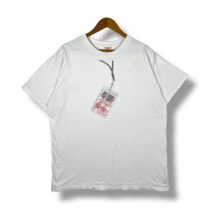 May include: White short-sleeved t-shirt with a graphic of a red and white backstage pass with the text "On Tour With The Boss" hanging from a black lanyard.