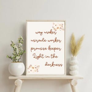 May include: A framed print with a white background and brown text that reads "way maker, miracle worker, promise keeper, light in the darkness". The text is surrounded by a floral design.