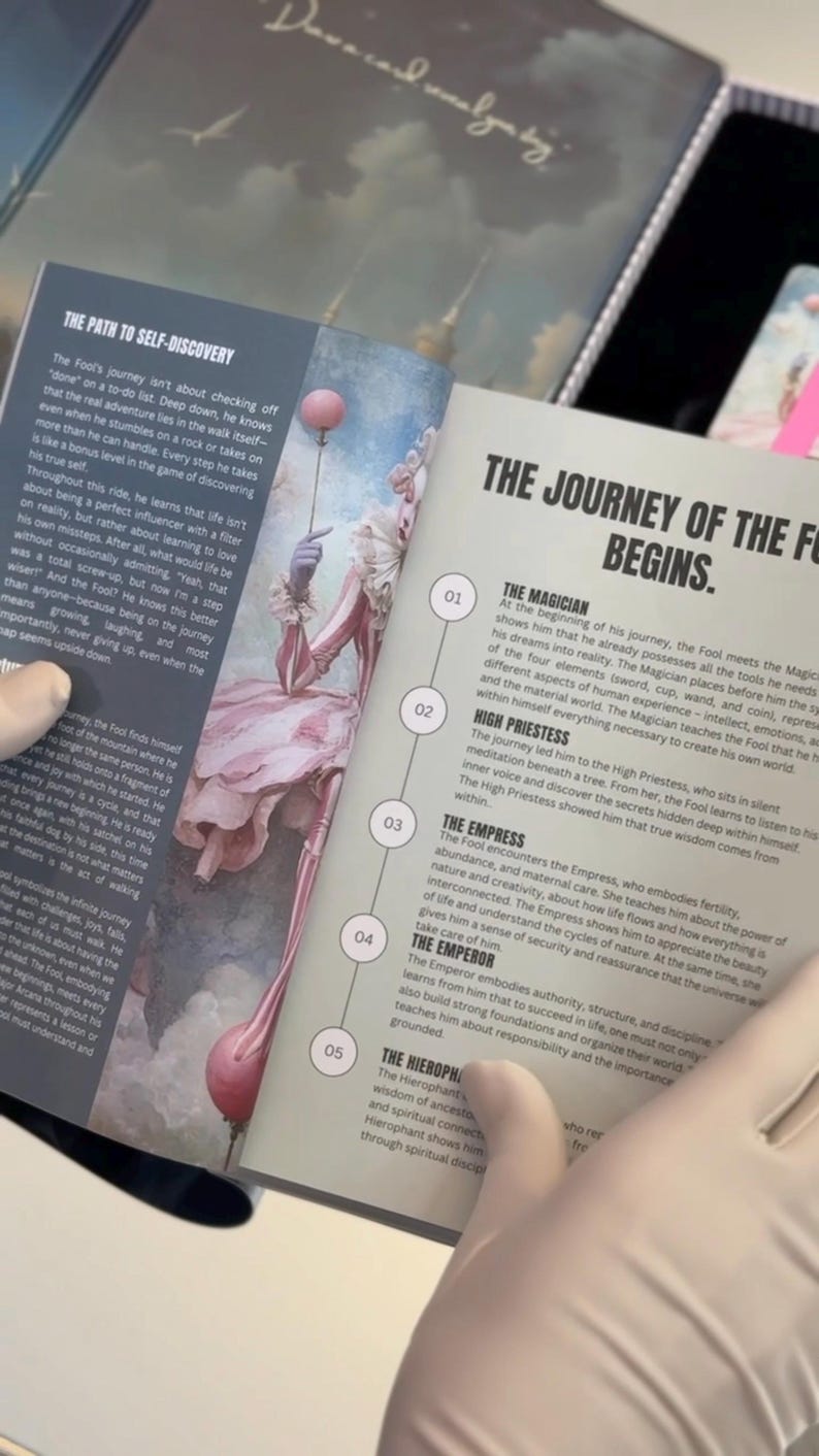 May include: An open book with the title "THE JOURNEY OF THE FOOL BEGINS" and illustrations of a tarot card deck. The pages describe the Fool's journey and the meaning of the Magician, High Priestess, Empress, Emperor, and Hierophant.