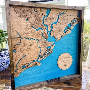 May include: A wooden map of Charleston Harbor, South Carolina, with a blue background and a circular wooden plaque that reads "Charleston Harbor 32.78&deg; North 79.93&deg; West".