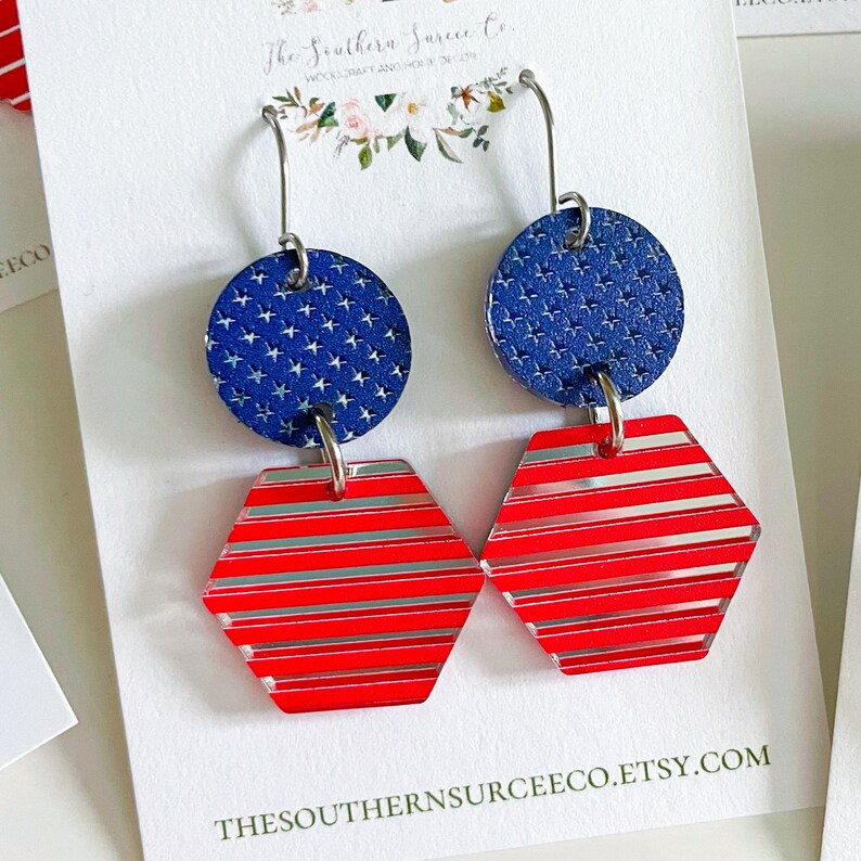 May include: Patriotic dangle earrings featuring a blue circle with white stars and a red and silver striped hexagon. The earrings are attached to silver hooks. The Southern Surcee Co. Etsy shop is visible.