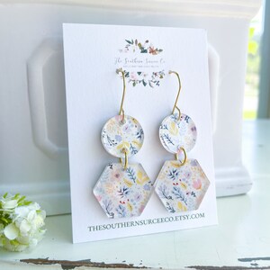 May include: Floral print earrings with gold-colored hooks. Each earring features a round top and a hexagon-shaped bottom. The earrings are on a white card with the text "The Southern Surcee Co." and "THESOUTHERNSURCEECO.ETSY.COM".