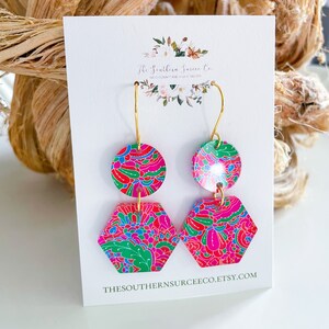 May include: A pair of dangle earrings with a vibrant floral pattern in pink, red, green, and blue. The earrings have a gold-colored hook and are composed of a circular top and a hexagonal bottom. The text "The Southern Surcee Co." and the Etsy shop URL are visible.