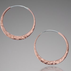 May include: A pair of hammered rose gold hoop earrings. The hoops are thick and have a textured surface.
