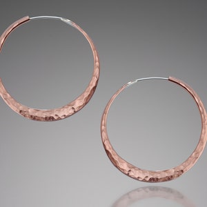 May include: A pair of hammered rose gold hoop earrings. The earrings are circular and have a textured surface.