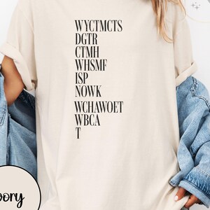 May include: Ivory-colored t-shirt with black text. The text includes a series of capitalized letter combinations. A denim jacket is draped over the shoulders. The word "ivory" is printed on a circular label.