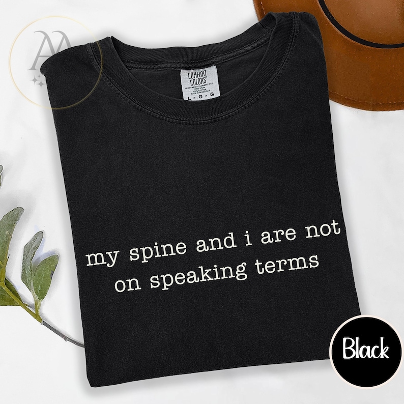 Pode incluir: Camiseta preta com o texto branco "my spine and i are not on speaking terms". A camisa tem gola redonda e uma etiqueta que diz "Comfort Colors". Um c&iacute;rculo preto com a palavra "Black" est&aacute; no canto inferior direito.
