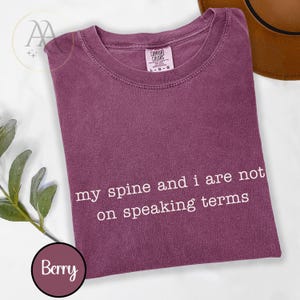 Pode incluir: T-shirt cor de baga com o texto branco "my spine and i are not on speaking terms". A camisa tem gola redonda e mangas curtas. A etiqueta "Comfort Colors" &eacute; vis&iacute;vel.