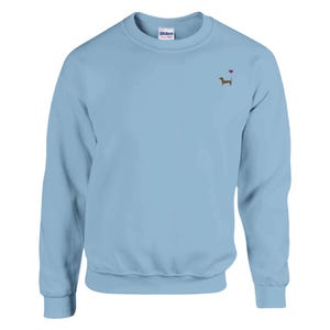 Könnte beinhalten: Ein hellblauer Pullover mit einem kleinen gestickten Dackel und einem roten Herzen darüber.