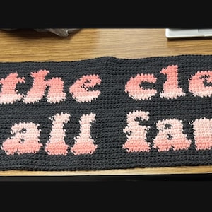 May include: A black crocheted banner with the words "In the clerb, We all fam." in pink and orange lettering.