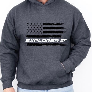 May include: A dark gray hooded sweatshirt with a distressed American flag design and the text "EXPLORER ST" in white.
