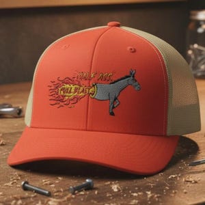 May include: A red and beige trucker cap with an embroidered design. The design features a cartoon donkey with the text "Whole Ass Full Blast". The hat is on a wooden workbench.