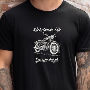 May include: Black t-shirt featuring a motorcycle graphic with the text "Kickstands Up Spirits High" in white script. The motorcycle is a detailed black and white illustration. The shirt is made of a soft material.