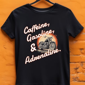May include: Black t-shirt featuring a motorcycle graphic inside a red circle. The shirt has the words "Caffeine, Gasoline, & Adrenaline" in a stylized font. The design is centered on the front of the shirt.