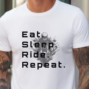 May include: White t-shirt with the text "Eat. Sleep. Ride. Repeat." in black block letters. A black and gray graphic of a motorcyclist on a motorcycle is centered between the words. The shirt has short sleeves.
