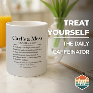 May include: White ceramic mug with the text "Carl's a Mess" and a definition. The mug also has the phrases "Treat Yourself" and "The Daily Caffeinator" printed on it. A glass vase with green stems and an open book are in the background.