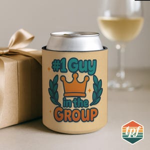 May include: A tan can cooler with the text "#1 Guy in the GROUP" in teal and orange, featuring a crown and laurel leaves. A silver can sits inside the cooler. A gift box and a wine glass are in the background.