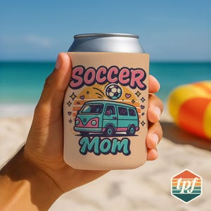 May include: A tan can cooler with the words "Soccer Mom" in pink and teal. The design includes a soccer ball, a teal and pink van, and orange and yellow accents. The cooler is held by a person on a beach.