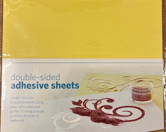 May include: A package of Silhouette double-sided adhesive sheets. The package contains eight 8.5" x 11" sheets. The package has a yellow background and features a sample design with glitter and decorative materials.