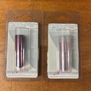 May include: Two etching tools in clear plastic packaging. The tools are metallic purple and cylindrical. The packaging has the words "Etching Tool" and the website address www.artisticcreativeproducts.com.