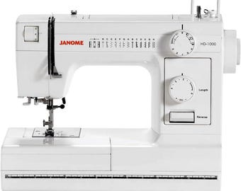 May include: A white Janome HD-1000 sewing machine. The machine features a variety of stitch options, a stitch length dial, and a reverse stitch button. The Janome logo is visible in red. The machine has a built-in ruler.