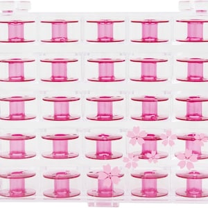 May include: A clear plastic sewing bobbin storage case filled with pink bobbins. The case has a grid of individual compartments, each holding a bobbin. Pink cherry blossom decals decorate the front of the case.