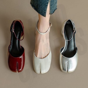 Op de afbeelding: Drie paar damesschoenen met hakken en enkelbandjes. De schoenen zijn in rood, wit en zilver. De schoenen hebben een unieke vierkante neusvorm.