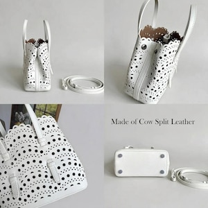 May include: A white leather handbag with a laser-cut design, featuring a top handle and a detachable shoulder strap. The bag has a rectangular base and a scalloped edge. The text "Made of Cow Split Leather" is visible.