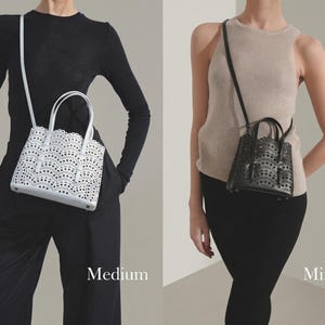 May include: Two handbags, a medium white and a mini black, are displayed. The white bag has a scalloped edge and intricate cut-out design. The black bag has a similar design. Both bags have top handles and adjustable shoulder straps. The word "Medium" and "Mini" are displayed.
