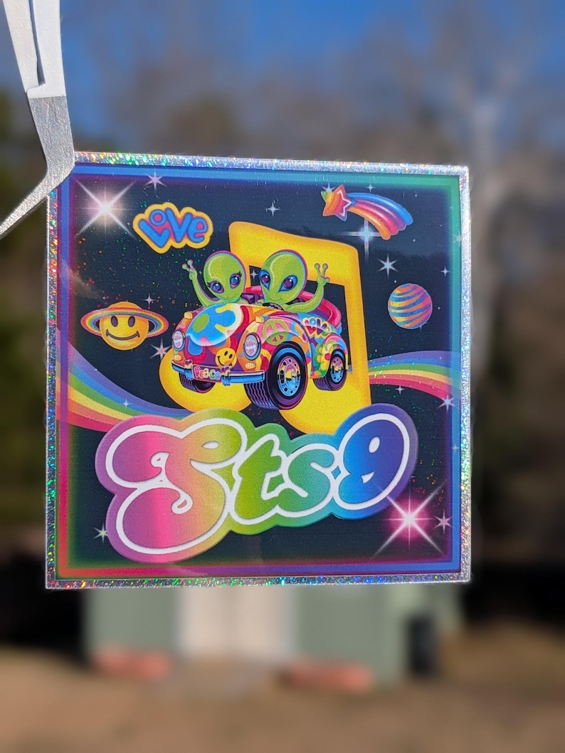 May include: Square sticker with a holographic border featuring a colorful cartoon design. Two green aliens are in a psychedelic car, with the text "sts9" in a rainbow font. Other elements include a rainbow, planets, and the word "love".