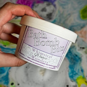 May include: A white container of "Bath Bomb Bits" with the text "Whimsical Water Wonders" on a purple label. The container is held in a hand, with a colourful, bubbly background.