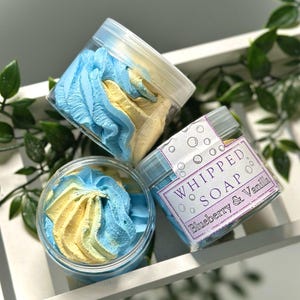 May include: Three jars of whipped soap, one with a blue and yellow swirl, one with a blue and yellow swirl, and one with a label that reads "Whipped Soap Blueberry & Vanilla".