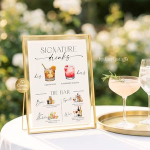 May include: A gold-framed sign with the words "Signature Drinks" and illustrations of cocktails. The sign includes the text "his" and "hers" with drink names. A gold tray holds two glasses, one with a sprig of rosemary.