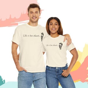 Puede incluir: Dos personas vestidas con camisetas color crema con el texto "Life is too short..." y un pequeño gráfico de un helado. Las camisetas se combinan con vaqueros azules. El fondo tiene pinceladas rosas, blancas y amarillas.