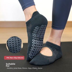 Puede incluir: Calcetines de yoga de color gris oscuro con suelas de silicona antideslizantes. Los calcetines tienen un diseño recortado y están etiquetados como "YOGA SOCKS". La imagen también incluye un primer plano del patrón de la suela y texto que indica la idoneidad para aeróbic, salto de cuerda, fitness, yoga, Pilates y danza.
