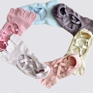 May include: A collection of toe socks in various pastel colors, including pink, blue, and lavender. Each sock features a unique design with individual toe slots and crisscross straps across the top, creating a ballet-inspired look. The socks are arranged in a circular pattern.