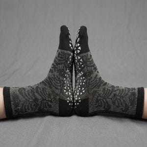 Puede incluir: Dos calcetines grises y negros con un estampado floral y puntos de agarre blancos en las suelas. Los calcetines se muestran sobre un fondo gris. La palabra "socks" es visible en la suela.