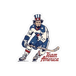 May include: A sticker featuring a cartoon illustration of a hockey player dressed as Uncle Sam. The player wears a white and blue uniform with stars and stripes, a top hat, and the text "Team America" in red.