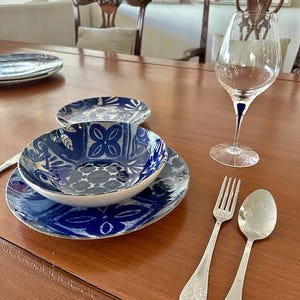 May include: A dining table setting with blue and white patterned plates and bowls. A wine glass, fork, and spoon are also on the table. The table is made of wood.