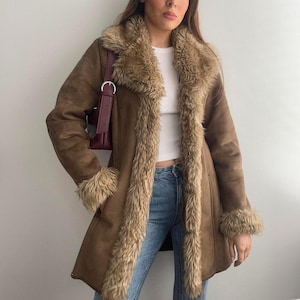 May include: A brown faux suede coat with a faux fur trim around the collar, cuffs, and down the front. The coat has a longline silhouette and a classic design. The coat is a warm, stylish outerwear option.