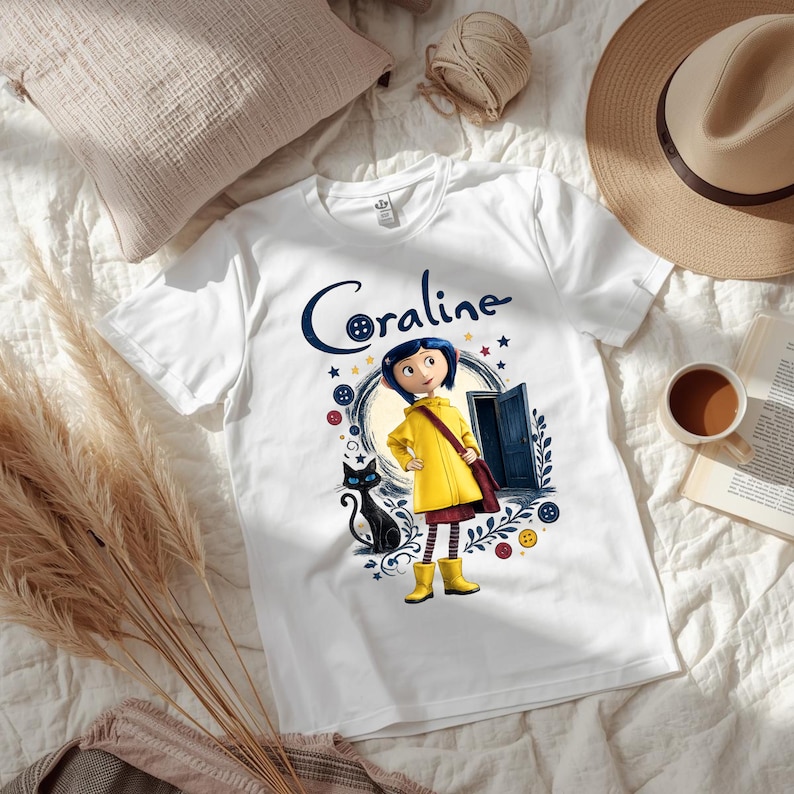 K&ouml;nnte beinhalten: Ein wei&szlig;es kurz&auml;rmeliges T-Shirt mit einem Grafikdruck der Figur Coraline, die einen gelben Regenmantel und Stiefel tr&auml;gt und neben einer schwarzen Katze steht. Das Design enth&auml;lt eine blaue T&uuml;r, bunte Kn&ouml;pfe, Sterne und den Schriftzug Coraline.