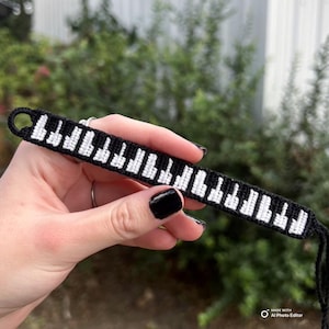 May include: Black and white friendship bracelet with a piano keyboard design.
