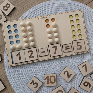 Pu&ograve; includere: Giocattolo educativo in legno con perline colorate e numeri. Il giocattolo mostra l'equazione 12 - 7 = 5.