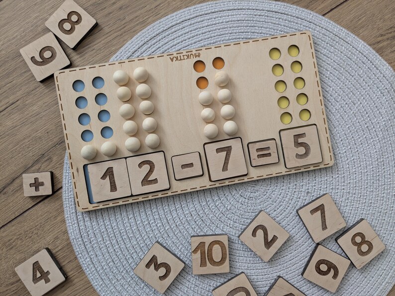 Pu&ograve; includere: Giocattolo educativo in legno con perline colorate e numeri. Il giocattolo mostra l'equazione 12 - 7 = 5.