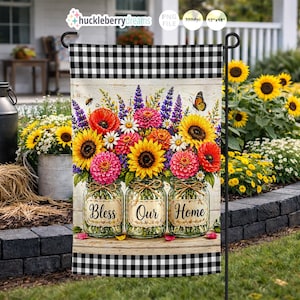 Puede incluir: Una bandera de jardín con un arreglo floral vibrante en tarros de cristal, con girasoles, amapolas y margaritas. La bandera tiene un borde a cuadros blanco y negro y las palabras "Bless Our Home".