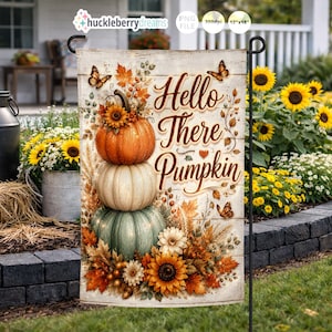 May include: A garden flag featuring a stack of three pumpkins in orange, cream, and green, adorned with sunflowers and fall foliage. The flag reads "Hello There Pumpkin" in elegant script, with butterflies scattered around the design. The flag is 12"x18".