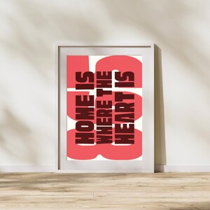 May include: A white framed print with a pink background and the text "HOME IS WHERE THE HEART IS" in dark red.