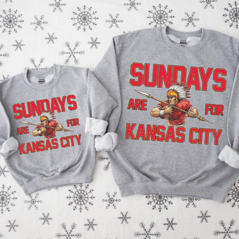 Two gray sweatshirts with red text and graphics, one larger than the other, both featuring a cowboy or Indian-style character.
