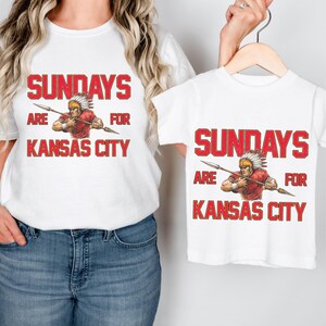 A woman wearing a white t-shirt with a graphic design and text, and a child wearing a smaller white t-shirt with a similar graphic design and text.
