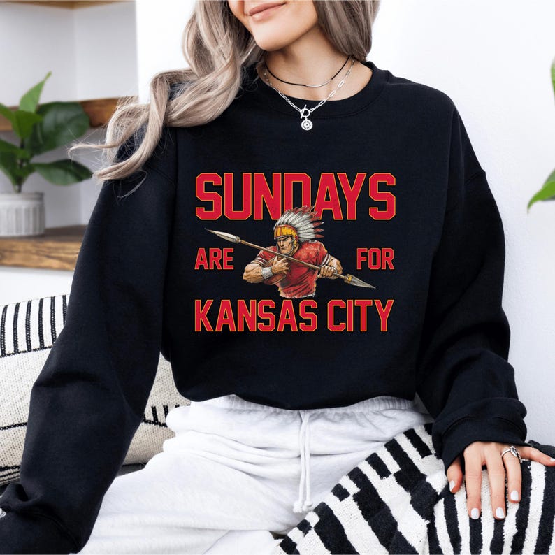 A woman wearing a black sweatshirt with a graphic design on it, which says "SUNDAYS ARE FOR KANSAS CITY".
